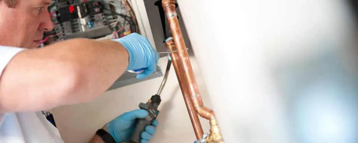 Water heater repair technician testing copper pipe connections and controls in Dayton, OH
