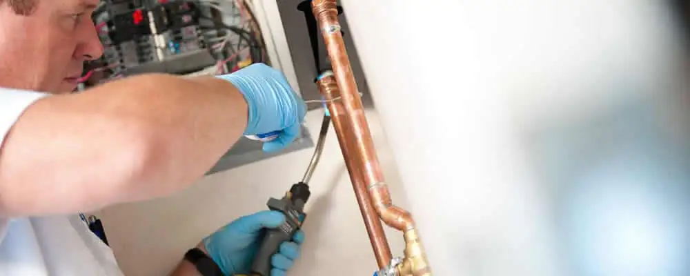 Water heater repair technician testing copper pipe connections and controls in Dayton, OH